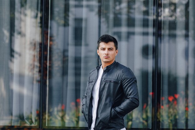 Chico con estilo joven con gafas en chaqueta de cuero negro sobre fondo de cristal