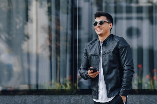 Chico con estilo joven con gafas en chaqueta de cuero negro con teléfono