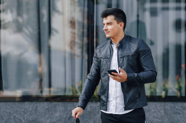 Chico con estilo joven con gafas en chaqueta de cuero negro con teléfono