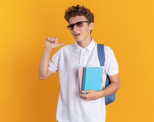 Chico estudiante en ropa casual con auriculares con gafas con mochila sosteniendo libros
