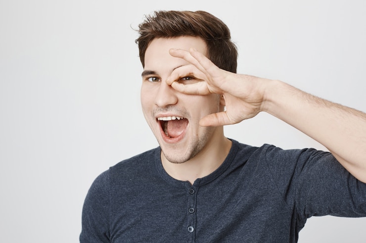 Foto gratuito chico feliz despreocupado mostrando bien gesto sobre los ojos y sonriendo