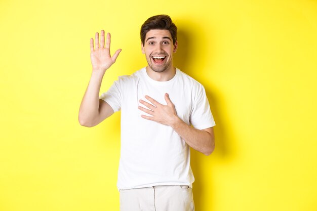 Chico feliz haciendo una promesa, sosteniendo la mano en el corazón, jurando decir la verdad, de pie sobre amarillo