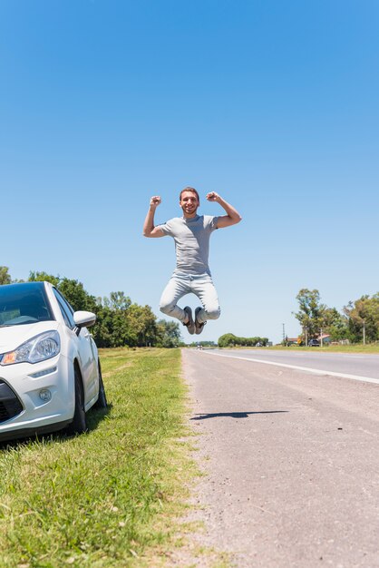 Chico feliz saltando en la carretera junto al coche