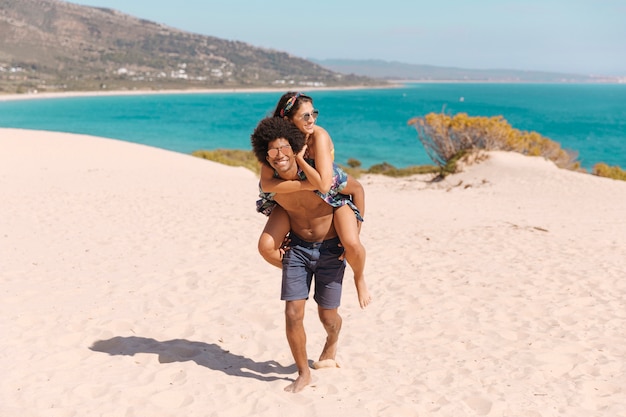 Chico feliz y sonriente con chica en la espalda en la playa