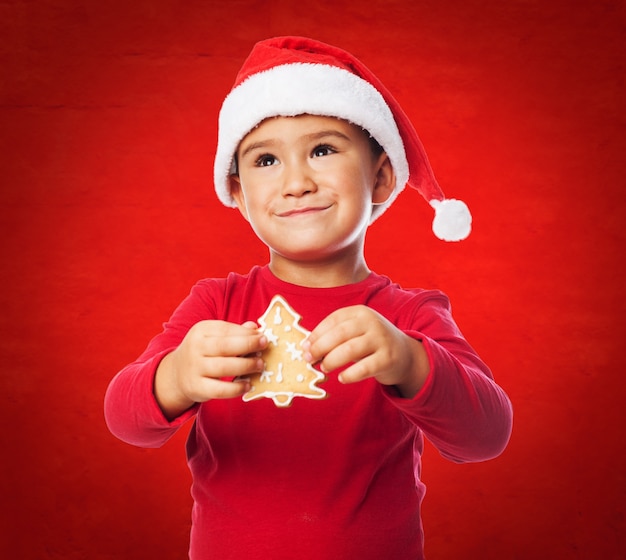 Foto gratuita chico con una galleta de árbol en un fondo rojo