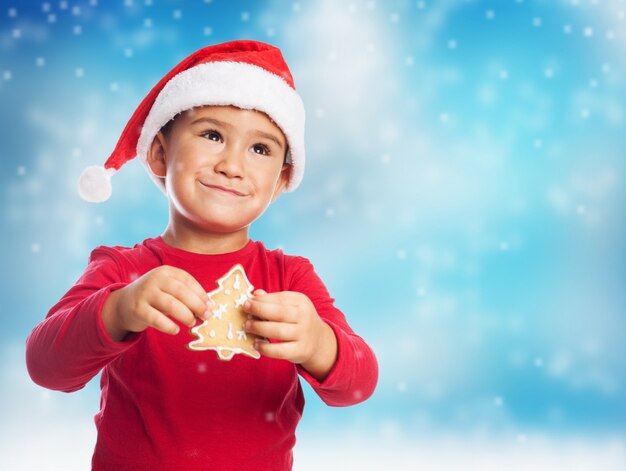 Chico con una galleta de árbol y sombrero de papa noel