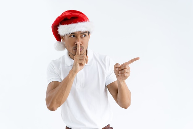 Chico con gorro de santa, apuntando a un lado y haciendo silencio gest