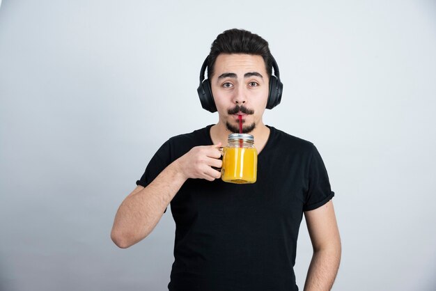 chico guapo en auriculares bebiendo de un vaso con jugo de naranja.
