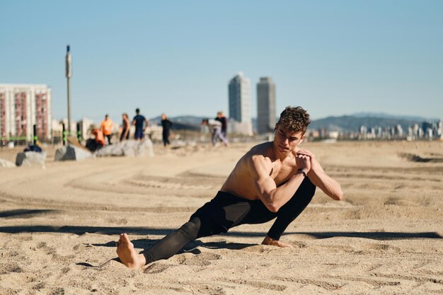 Chico guapo deportivo que se extiende durante el entrenamiento funcional en la playa de la ciudad. Hombre joven en forma en entrenamiento al aire libre