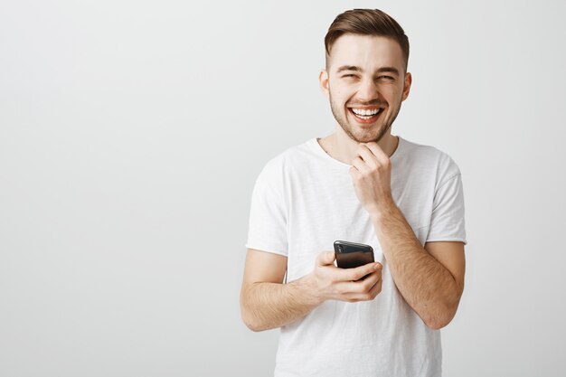 Chico guapo despreocupado riendo como usando la aplicación de teléfono móvil