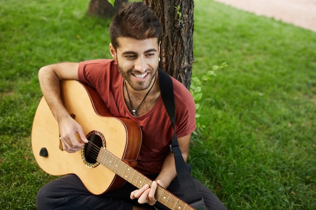 Chico guapo despreocupado tocando la guitarra en el parque