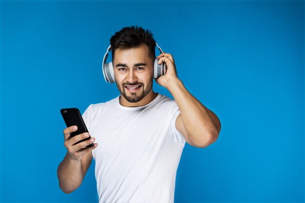 Chico guapo está escuchando música con auriculares y sosteniendo el teléfono celular en su brazo