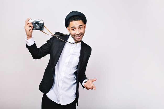 Chico guapo feliz en traje, sombrero divirtiéndose con la cámara. Emocionado, expresando verdaderas emociones positivas, sonriendo, viajando, fotógrafo, éxito.