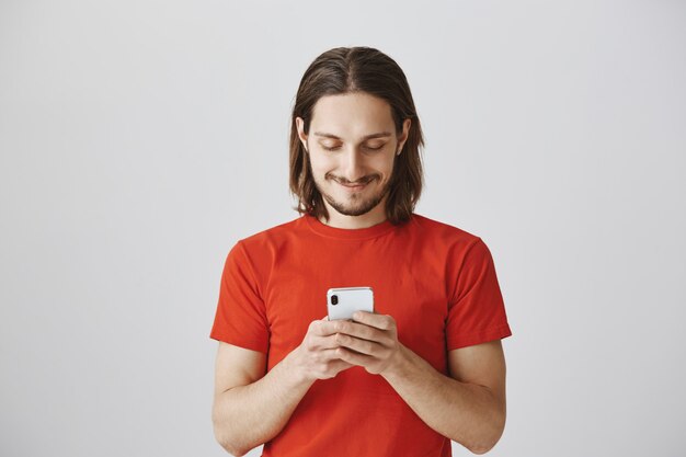 Chico guapo hipster en camiseta roja mediante teléfono móvil, mensajería