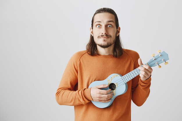 Chico guapo hipster tocando el ukelele y sonriendo