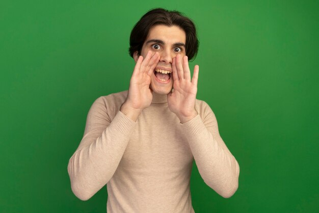 Chico guapo joven de aspecto alegre llamando a alguien aislado en la pared verde