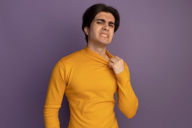 Chico guapo joven con calefacción vistiendo un suéter de cuello alto amarillo sosteniendo el collar aislado en la pared púrpura