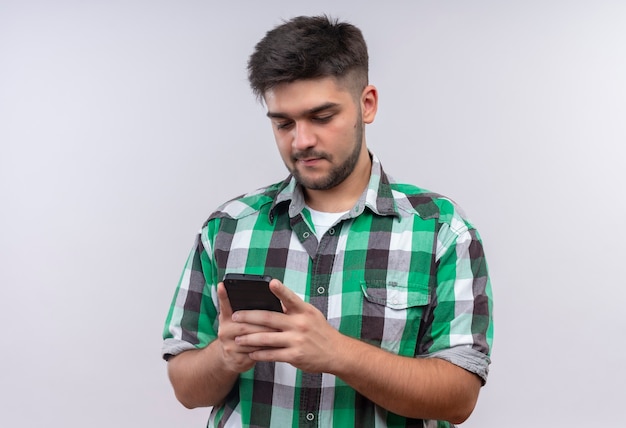 Chico guapo joven con camisa a cuadros charlando por teléfono con alguien tanding sobre pared blanca