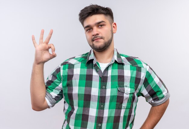 Chico guapo joven con camisa a cuadros haciendo bien firmar con los dedos de pie sobre la pared blanca