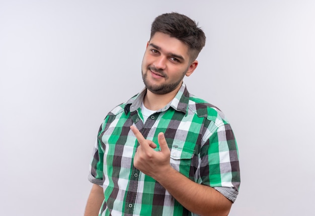 Chico guapo joven con camisa a cuadros mostrando signo de mierda con el dedo medio parado sobre la pared blanca