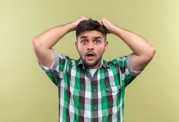 Chico guapo joven con camisa a cuadros sorprendido de pie sobre la pared de color caqui