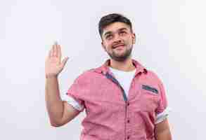 Foto gratuita chico guapo joven con camisa polo rosa haciendo dar mi signo de palabra con la mano izquierda levantada de pie sobre la pared blanca