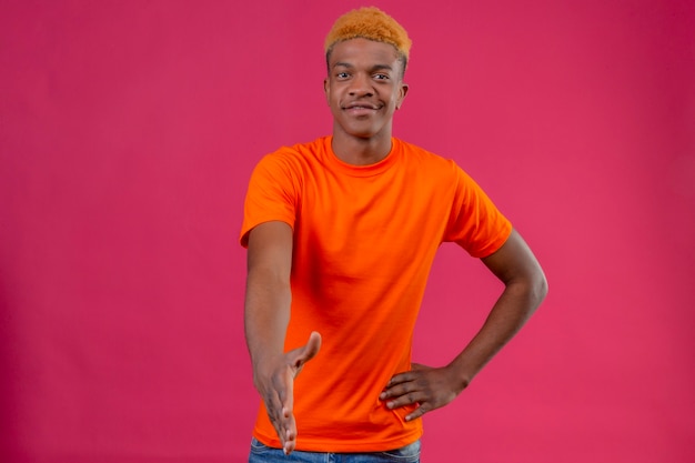 Chico guapo joven con camiseta naranja sonriendo amable haciendo gesto de saludo