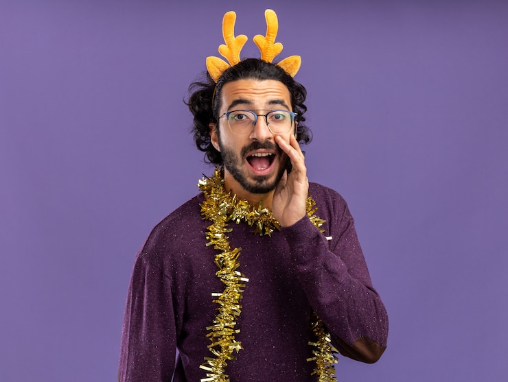 Foto gratuito chico guapo joven complacido con aro de pelo de navidad con guirnalda en el cuello llamando a alguien aislado sobre fondo azul.