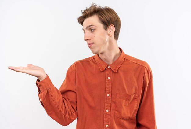 Chico guapo joven complacido con camisa roja fingiendo sostener y mirar algo aislado en la pared blanca