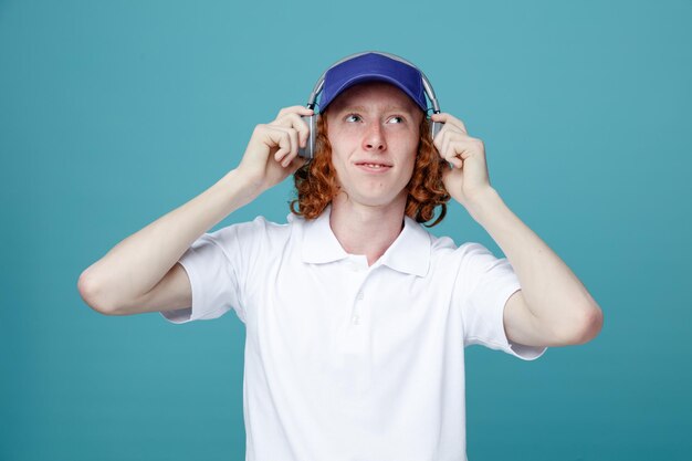 Chico guapo joven complacido en gorra usando auriculares aislados sobre fondo azul