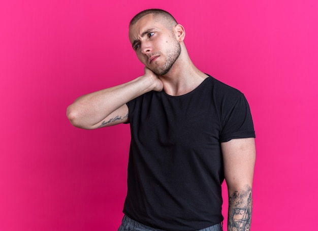 Foto gratuita chico guapo joven disgustado con camiseta negra poniendo la mano en el cuello dolorido aislado en la pared rosa