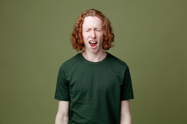 Chico guapo joven enojado con camiseta verde aislado sobre fondo verde