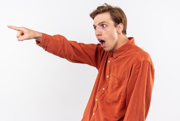 Chico guapo joven de lado mirando sorprendido con puntos de camisa roja en el lado