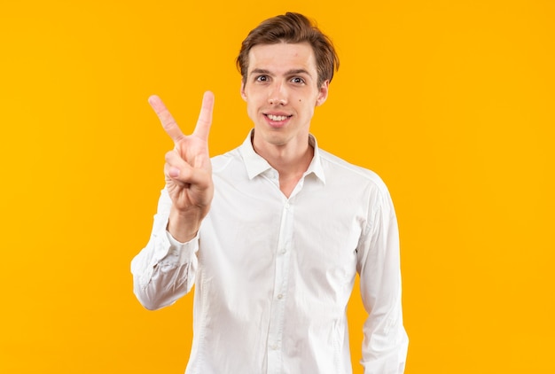 Chico guapo joven sonriente con camisa blanca mostrando dos aislados en la pared naranja