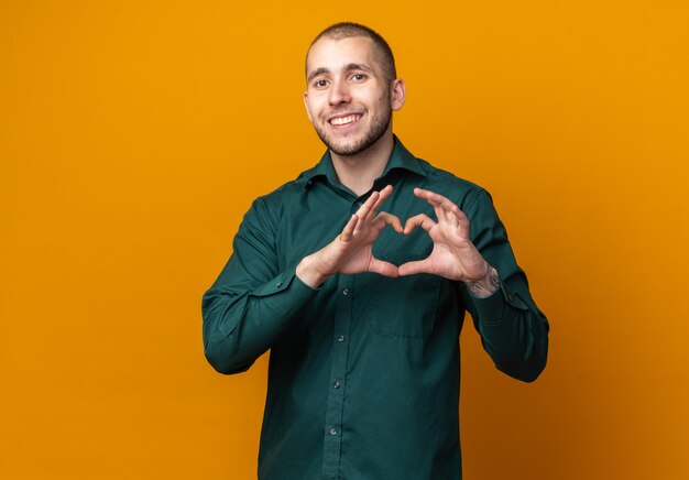 Chico guapo joven sonriente con camisa verde mostrando gesto de corazón