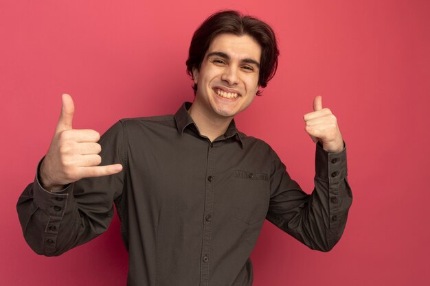 Foto gratuita chico guapo joven sonriente con camiseta negra que muestra el gesto de llamada telefónica aislado en la pared rosa