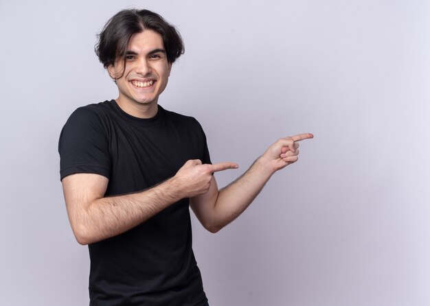 Chico guapo joven sonriente con puntos de camiseta negra en el lado aislado en la pared blanca con espacio de copia