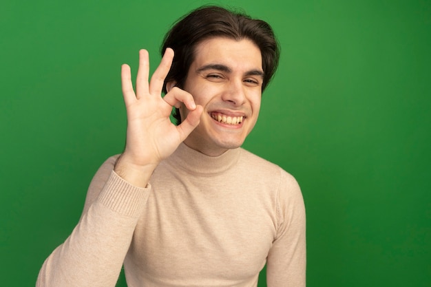 Chico guapo joven sonriente que muestra un gesto bien aislado en la pared verde