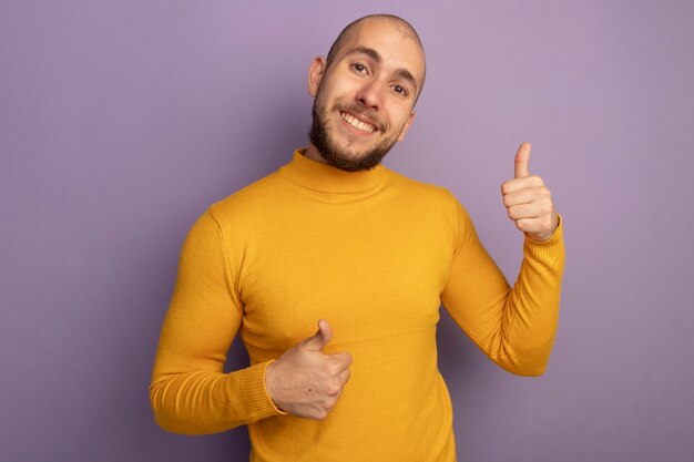 Chico guapo joven sonriente que muestra los pulgares para arriba aislado en la pared púrpura