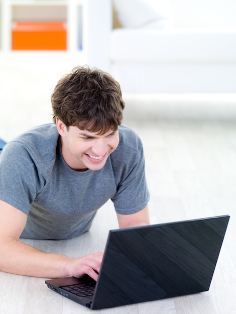 Chico guapo joven con sonrisa feliz escribiendo en la computadora portátil - en el interior