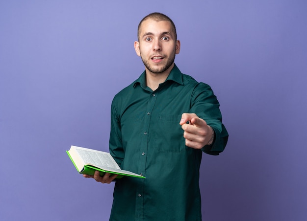 Foto gratuita chico guapo joven sorprendido con camisa verde sosteniendo puntos de libro en la parte delantera