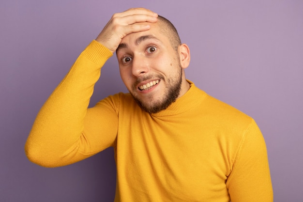 Chico guapo joven sorprendido poniendo la mano en la frente aislada en la pared púrpura