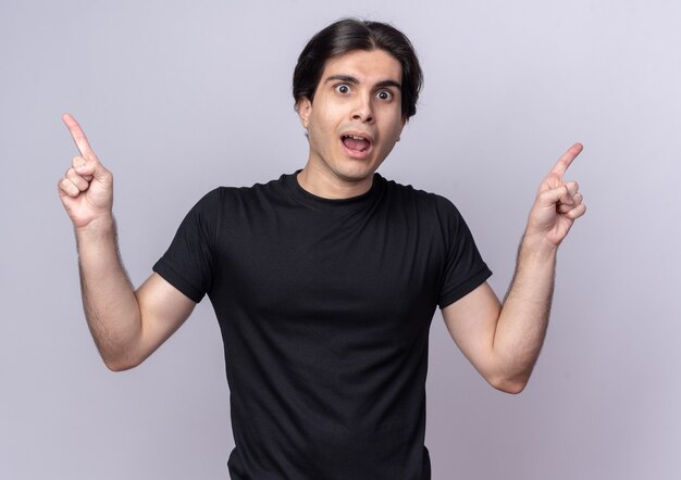 Chico guapo joven sorprendido con puntos de camiseta negra en diferentes lados aislados en la pared blanca