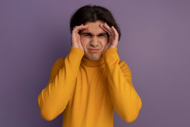 Chico guapo joven con suéter de cuello alto amarillo poniendo las manos alrededor de los ojos aislados en la pared púrpura