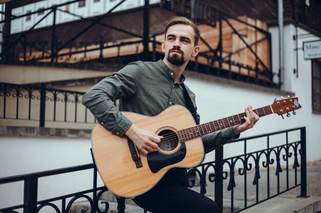 chico guapo joven toca la guitarra, recoge un acorde, músico callejero