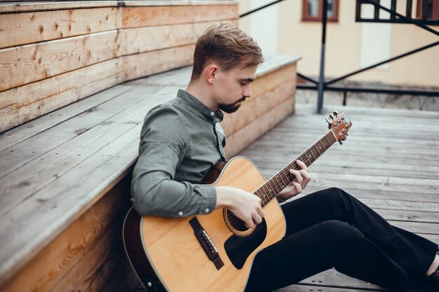 chico guapo joven toca la guitarra, recoge un acorde, músico callejero