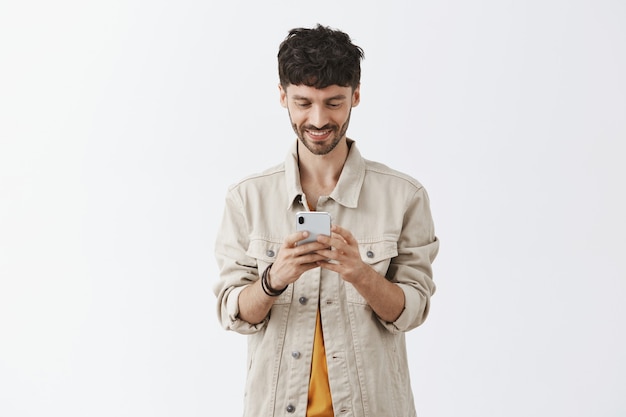 Foto gratuita chico guapo moderno con teléfono móvil y sonriendo