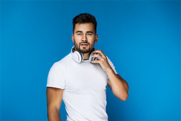 El chico guapo preguntado con auriculares en el cuello los sostiene con una mano