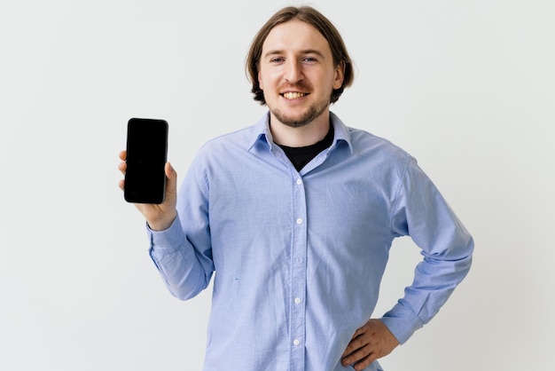 Chico guapo señalando con el dedo el teléfono de pantalla vacía sobre fondo blanco.