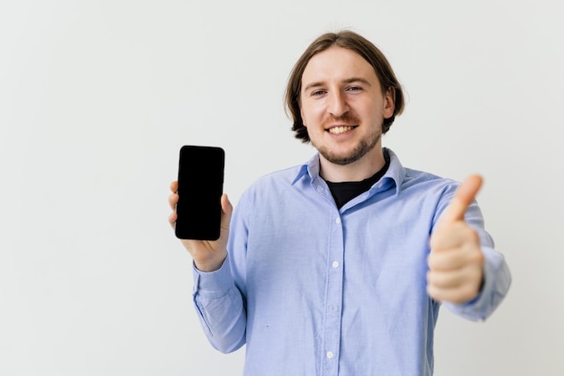 Chico guapo señalando con el dedo el teléfono de pantalla vacía sobre fondo blanco.